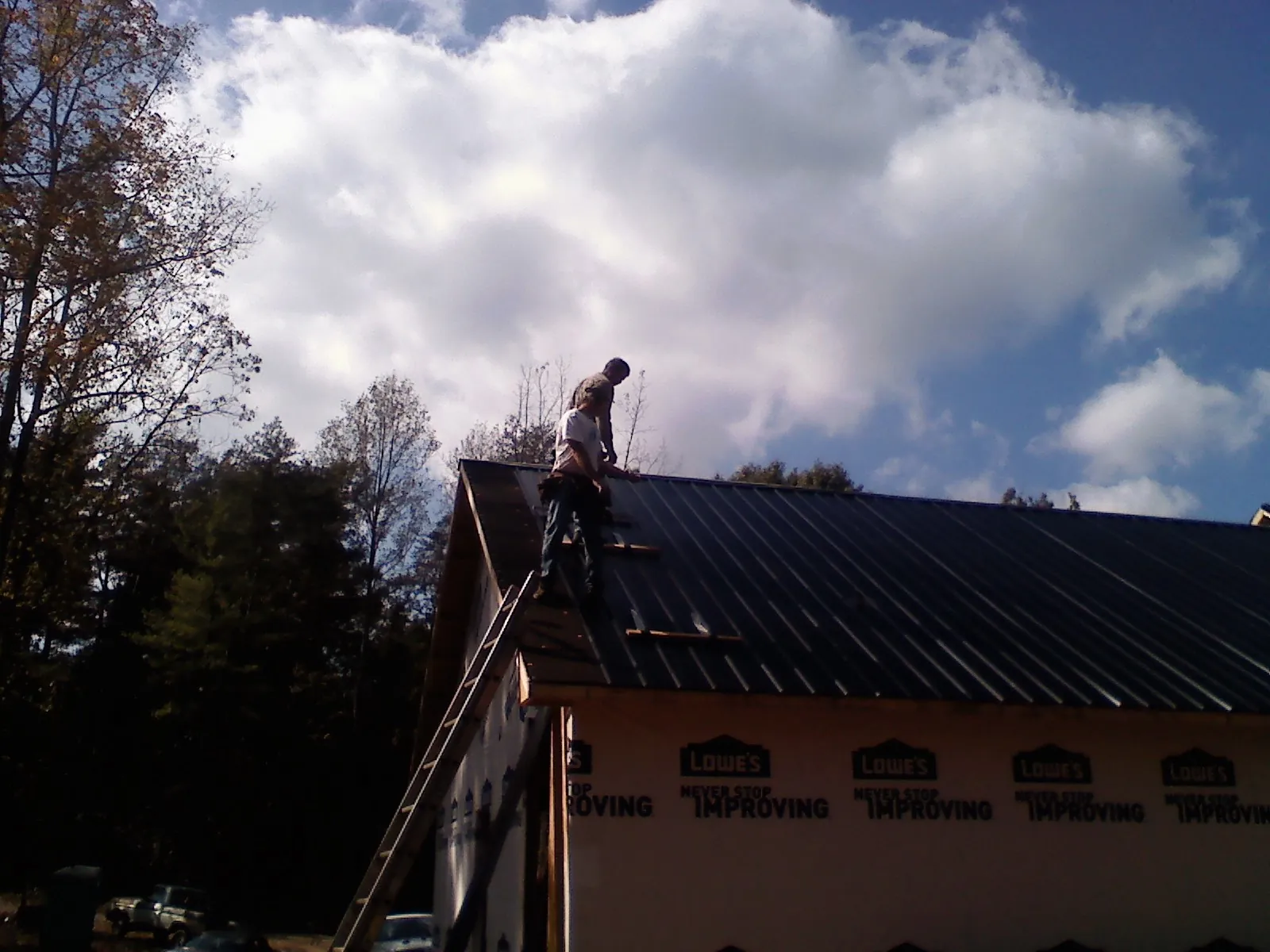 Roofer fastening dark metal panels high against a cloudy sky, from a Roof Inspection job in Somerdale