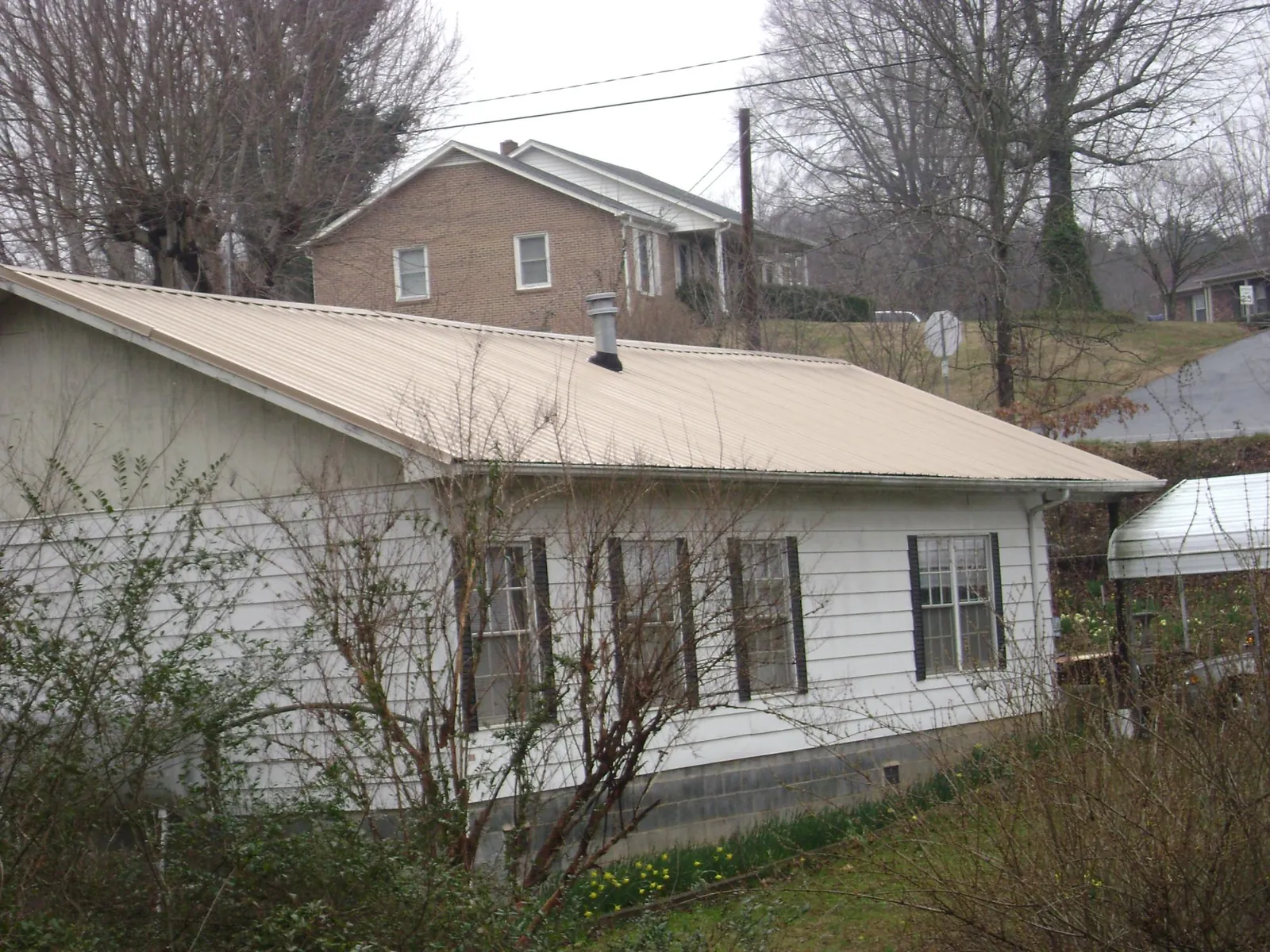 Tan metal roof on a white sided house set into a hillside — Commercial Roofing by Roofing Brothers in Somerdale